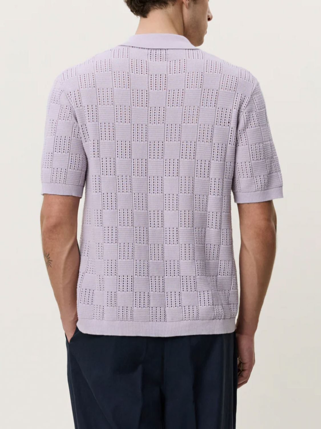 A person with short brown hair is seen from behind, wearing the Les Deux Squared Knitted SS Shirt in light purple and dark navy trousers against a plain, light background.