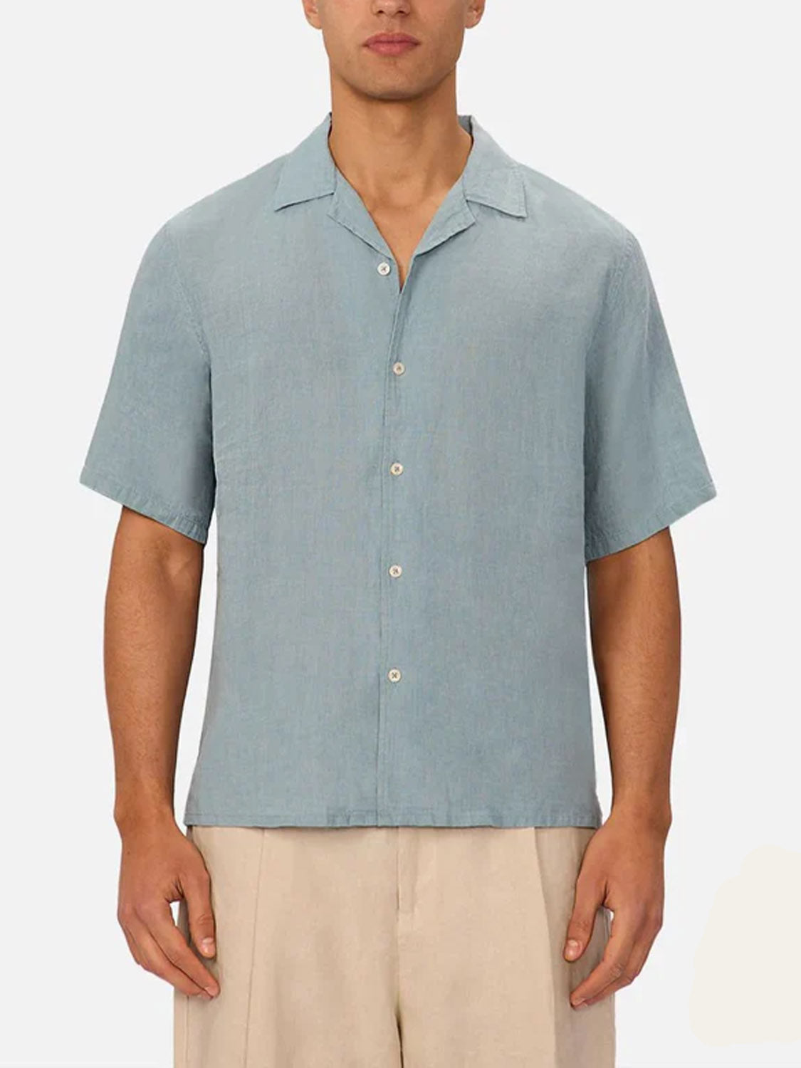 A man in the Industrie St Martins Short Sleeve Shirt, a light blue linen collared shirt, styled smart casually with beige shorts, stands against a plain white background.