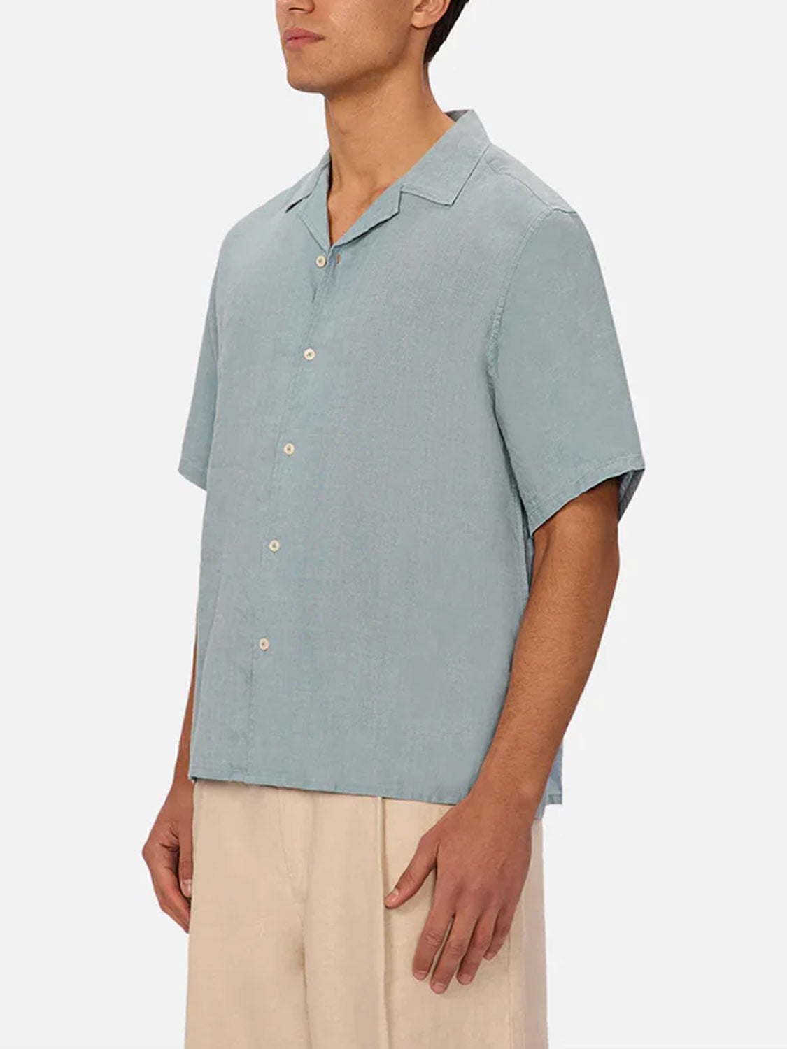 A person models Industrie’s The St Martins Short Sleeve Shirt in light blue with beige pants, standing mid-thigh up against a white background and facing slightly to the side.