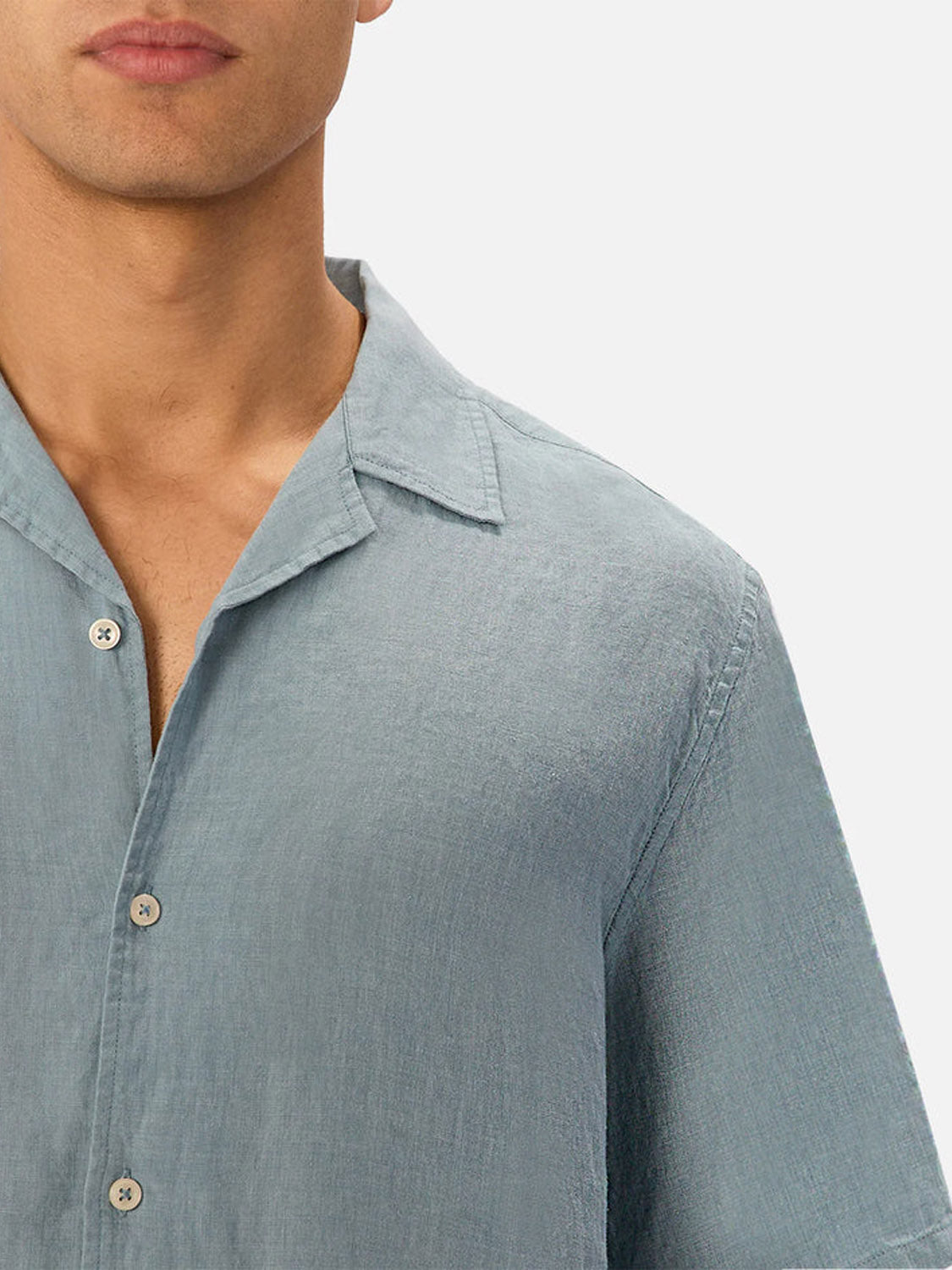 A close-up of a person wearing Industrie’s The St Martins Short Sleeve Shirt in light blue linen, featuring a collar and smart casual style, shown from nose to chest against a plain light background.