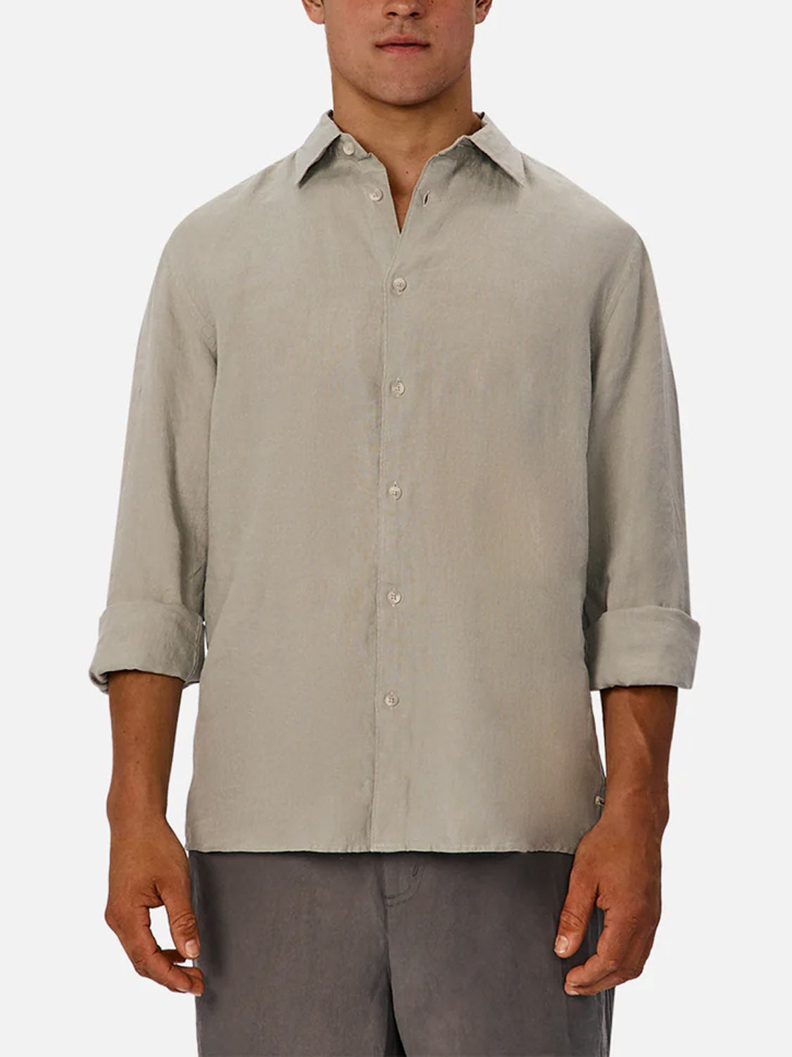 A man wears Industrie’s The St Martins Long Sleeve Shirt in light beige with rolled-up sleeves and gray pants, standing against a white background for a smart casual look.