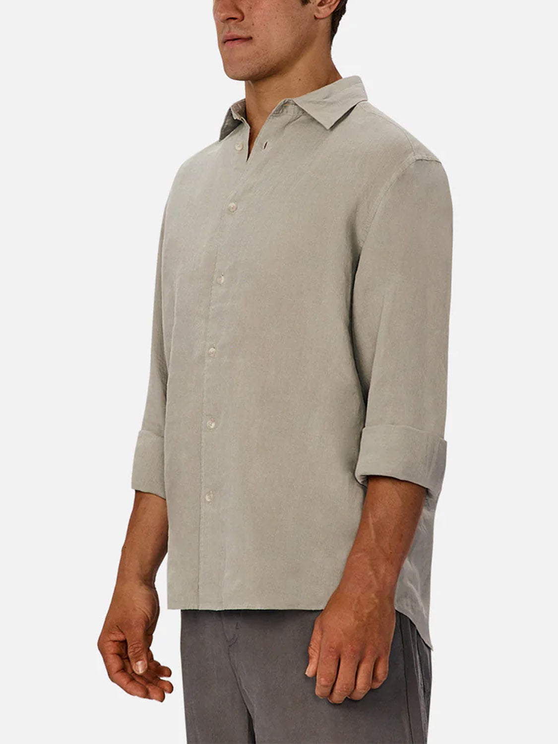 A man wears Industrie’s The St Martins Long Sleeve Shirt in light grey, sleeves rolled to the forearms, paired with grey pants, standing against a plain white background.