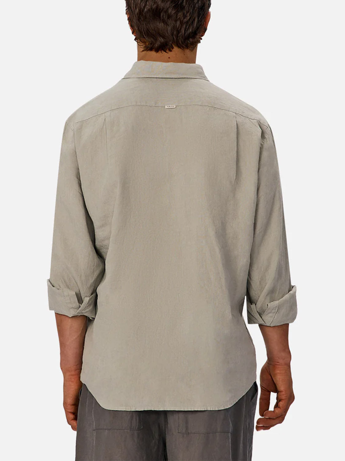 A person is seen from the back wearing Industrie’s The St Martins Long Sleeve Shirt in light gray with rolled-up sleeves, paired with gray shorts. The shirt has a relaxed fit, smart casual style, and features a small tag at the upper back.