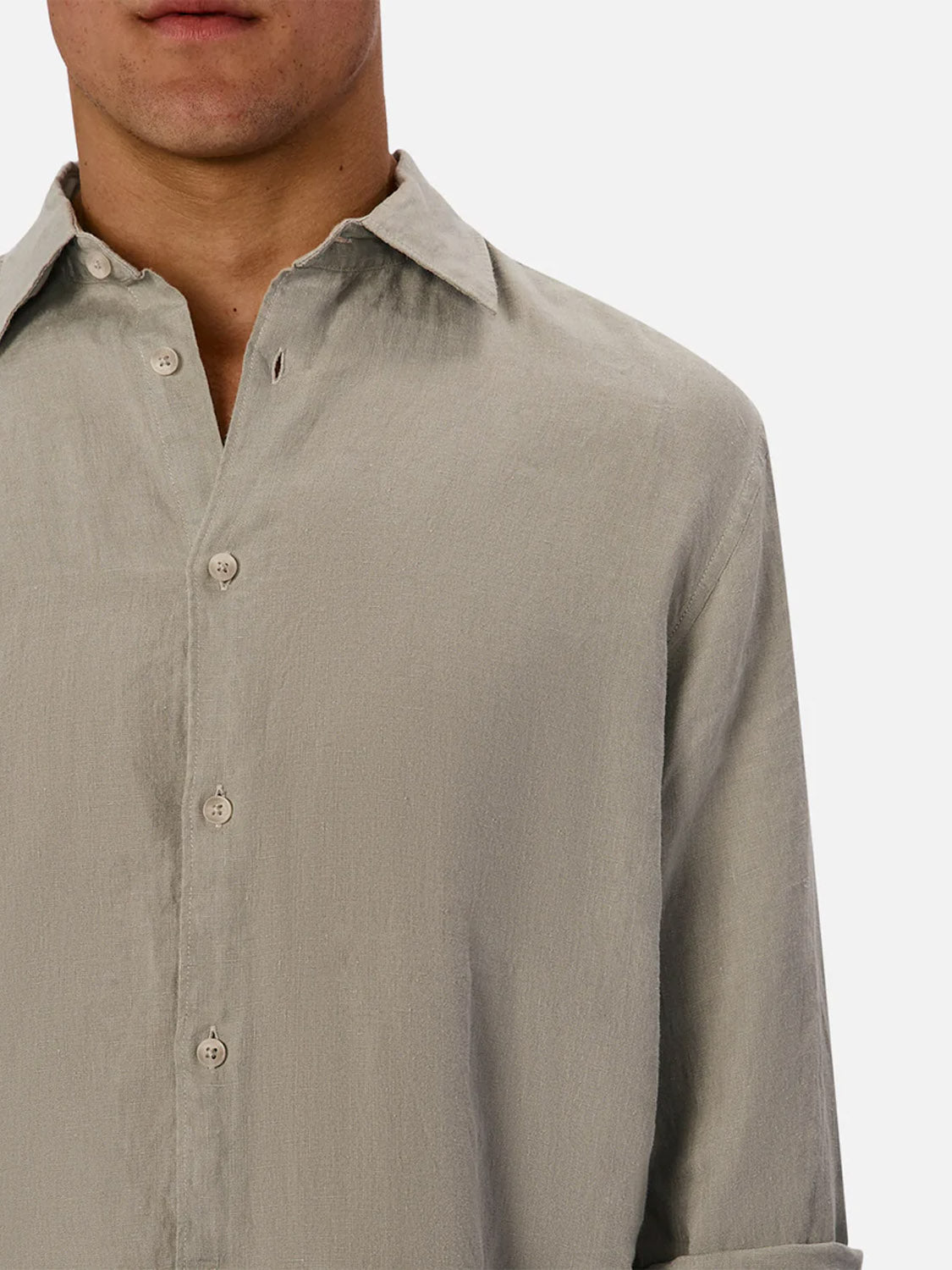 A person wears The St Martins Long Sleeve Shirt by Industrie in smart casual style. The light gray, soft-textured linen shirt is partially unbuttoned at the top, with only the lower half of their face visible.