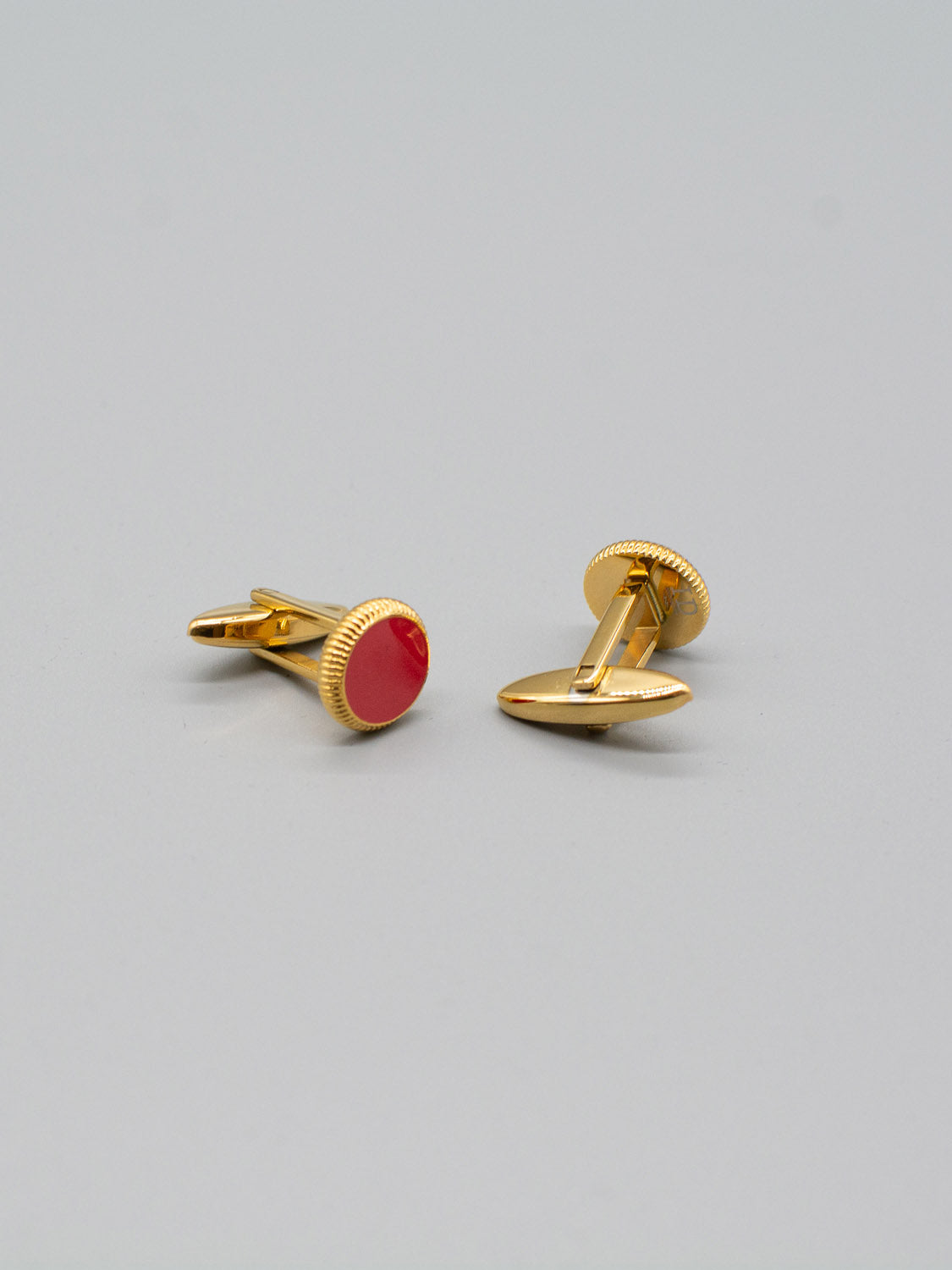 The Gold Plated Steel Enamel Cufflinks by ID Menswear feature red oval-shaped tops on a gray base, displayed at different angles to show both the decorative front and fastening mechanism—ideal for adding elegance to any formal attire.