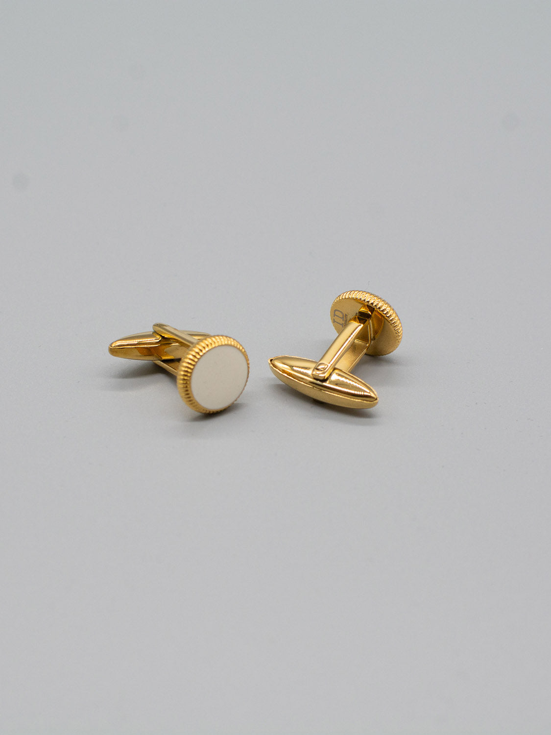The Gold Plated Steel Enamel Cufflinks from ID Menswear, featuring smooth round faces and textured edges, are perfect for formal attire and set against a plain light gray background.