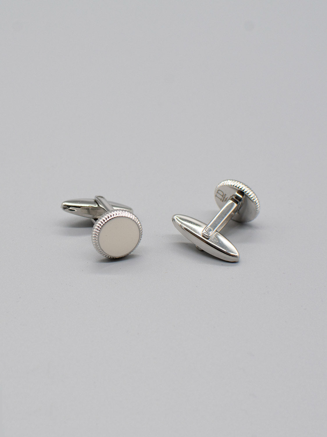 A pair of ID Menswear Rhodium Plated Steel Enamel Cufflinks with round, smooth surfaces on a light gray background featuring a bullet back mechanism and positioned at different angles to showcase their reflective finish and simple design.