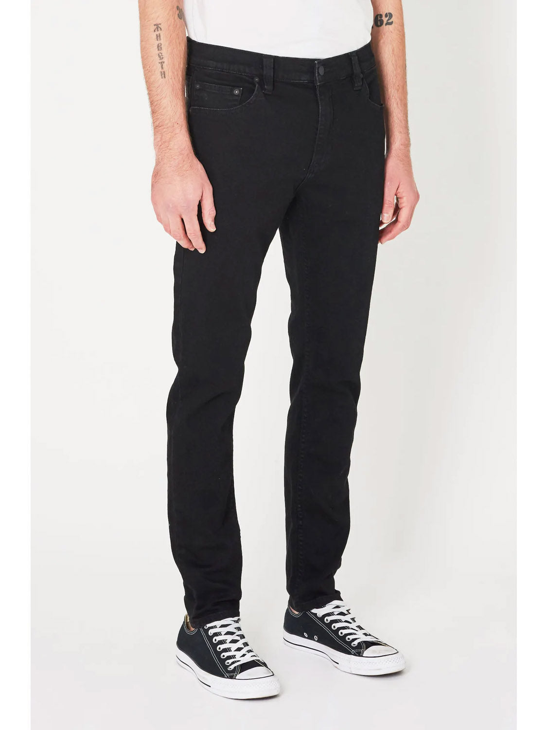 Someone wearing Rollas Stinger Black Gold super stretch denim skinny jeans and black low-top sneakers with white soles, shown from the waist down against a plain white background.