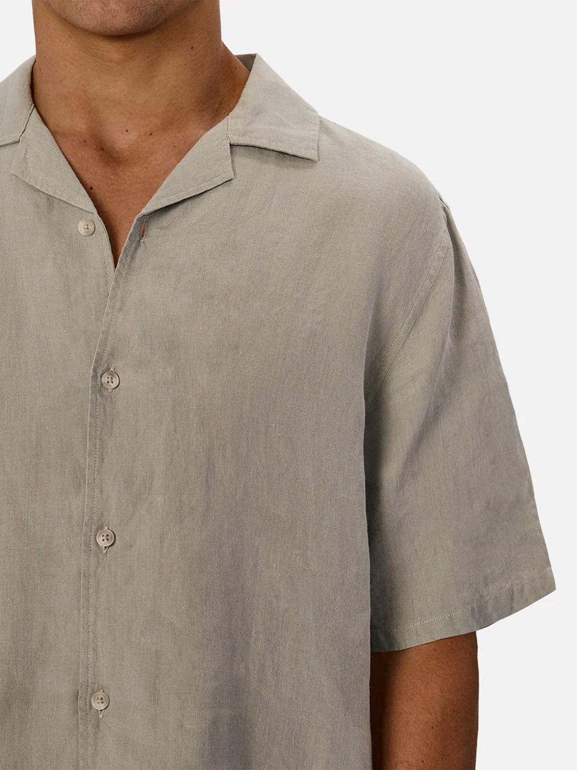 A person wears the Industrie St Martins Short Sleeve Shirt in light beige linen, featuring a collar and relaxed fit. The simple design suits smart casual looks. Only the upper torso and part of an arm are visible.