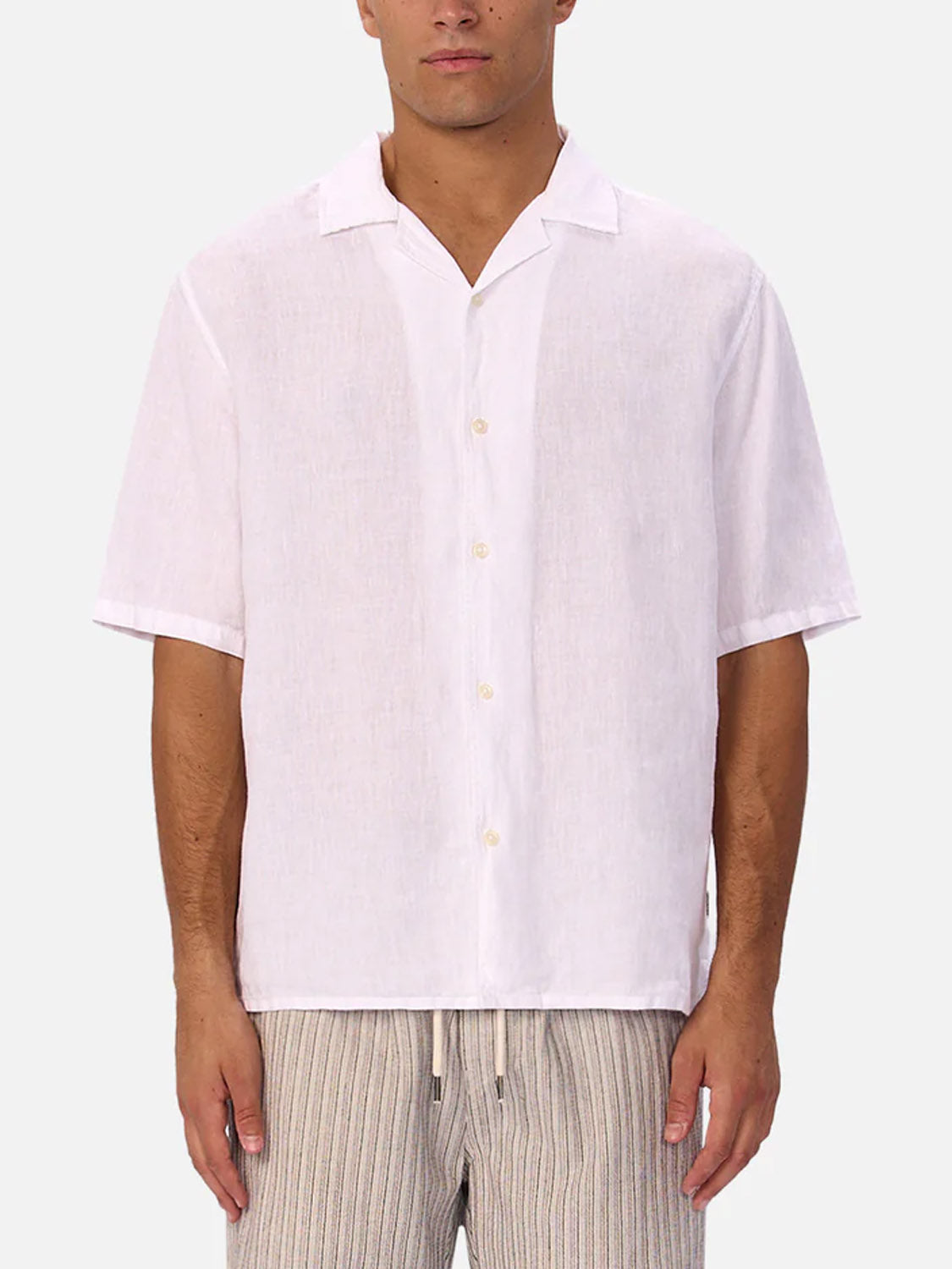 A person wearing Industrie’s The St Martins Short Sleeve Shirt in white, styled smart casual, with beige striped drawstring pants, stands against a light gray background.