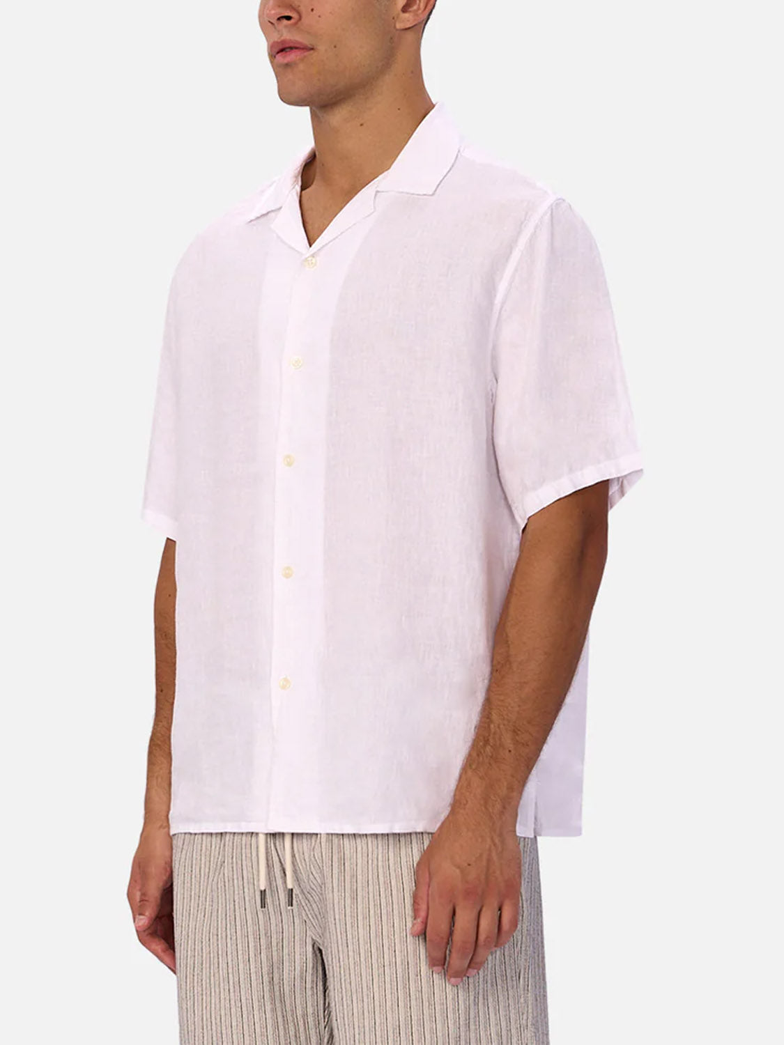 A man wearing Industrie’s The St Martins Short Sleeve Shirt and light-colored, vertically striped pants stands against a plain light gray background.