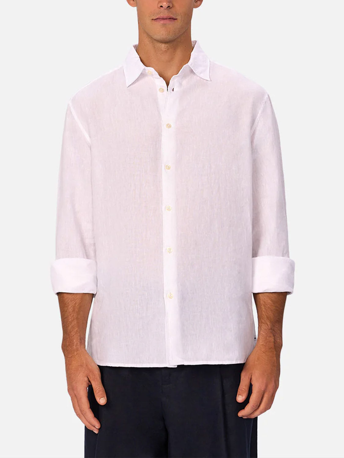 A man stands against a plain light background wearing the Industrie St Martins Long Sleeve Shirt with the sleeves rolled up, untucked, and paired effortlessly with dark pants for a smart casual look.