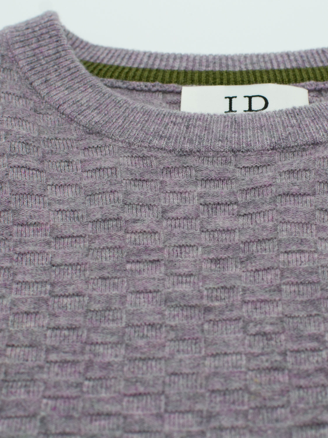 Close-up of a textured purple Stockholm Merino Wool Sweater by ID Menswear, featuring a waffle pattern. This lightweight piece has a classic crewneck with ribbed detailing and an ID tag inside.
