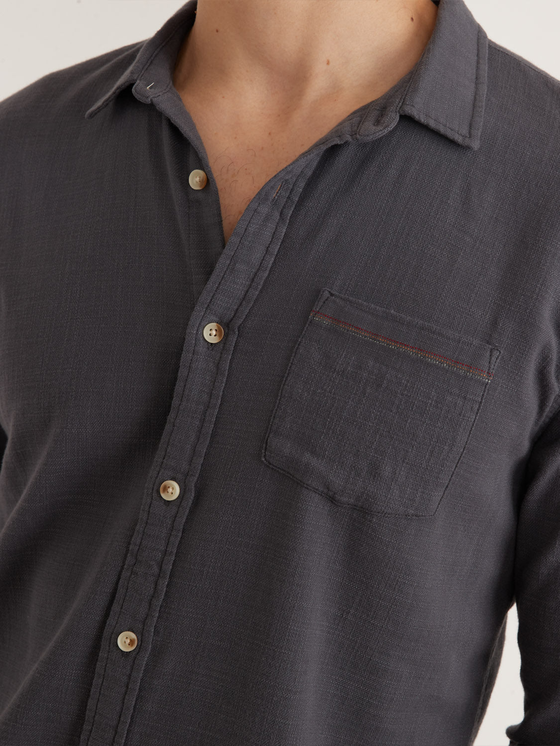The person is wearing the Marine Layer Stretch Selvage Long Sleeve Shirt, featuring a charcoal button-up design with beige buttons and a subtle red stitch on the left chest pocket, combining Marine Layers comfort and quality with classic style.