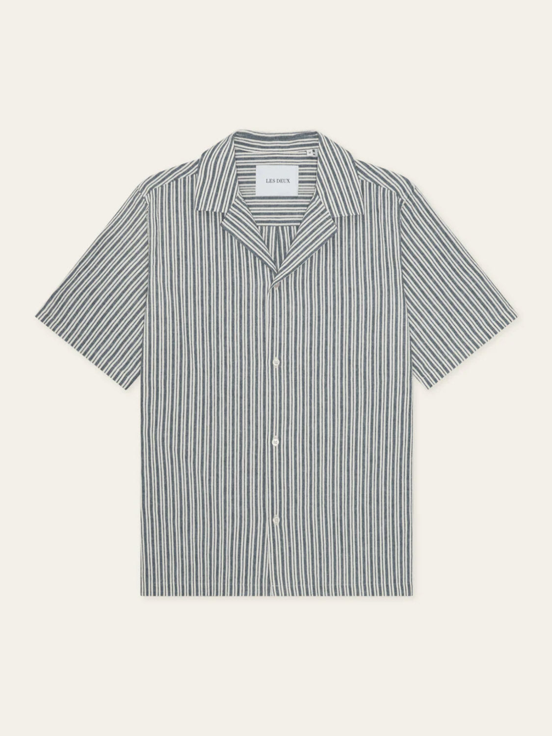 The Les Deux Stripe Cotton-Linen SS Shirt is a relaxed-fit, short-sleeved button-up with a camp collar and vertical black and white stripes on a light background, featuring a visible label inside the neckline.
