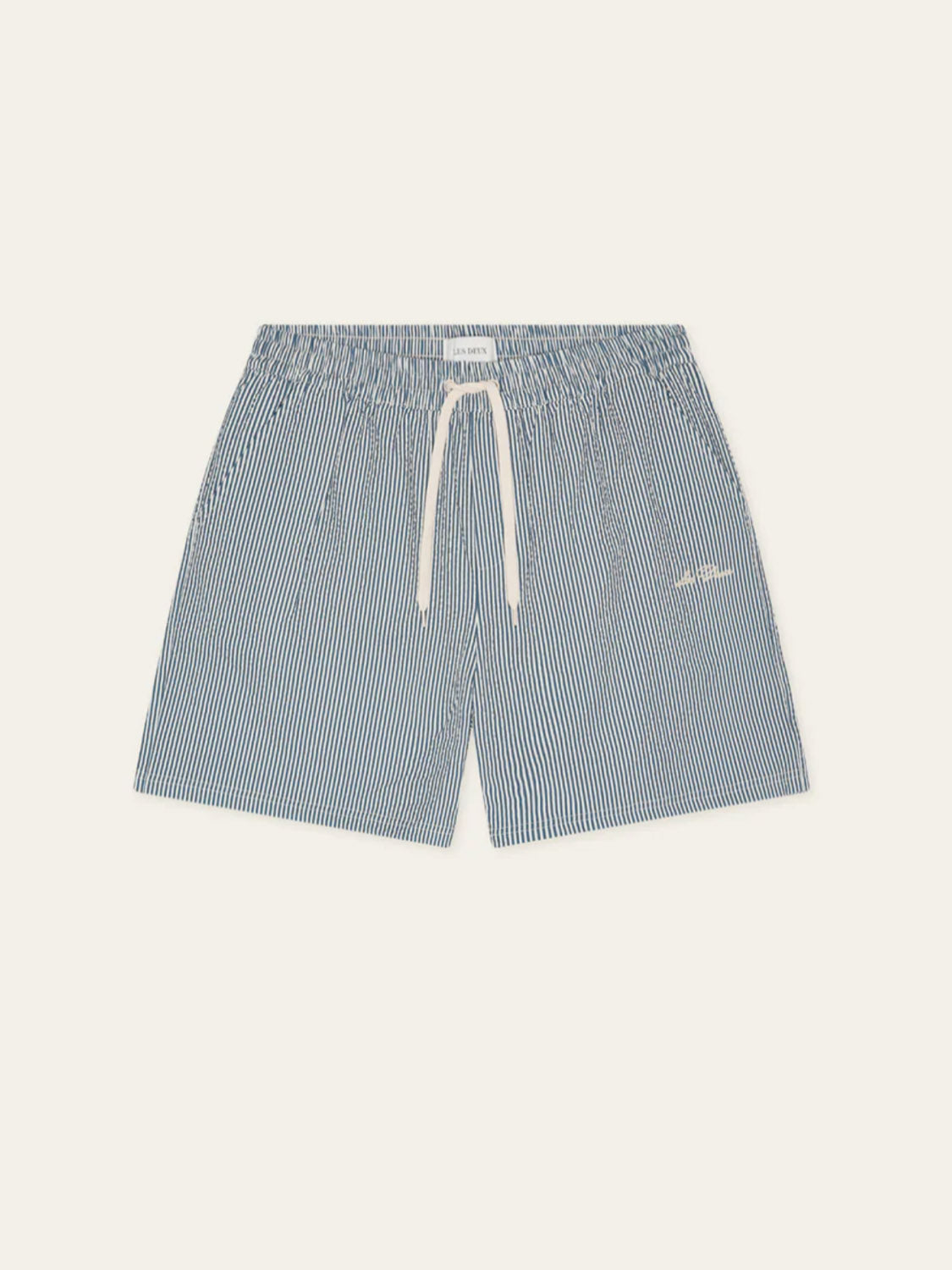 The Les Deux Stripe Seersucker Swim Shorts feature blue and white vertical stripes, an elastic waistband, white drawstring, and a small embroidered logo on the left leg for a classic look.