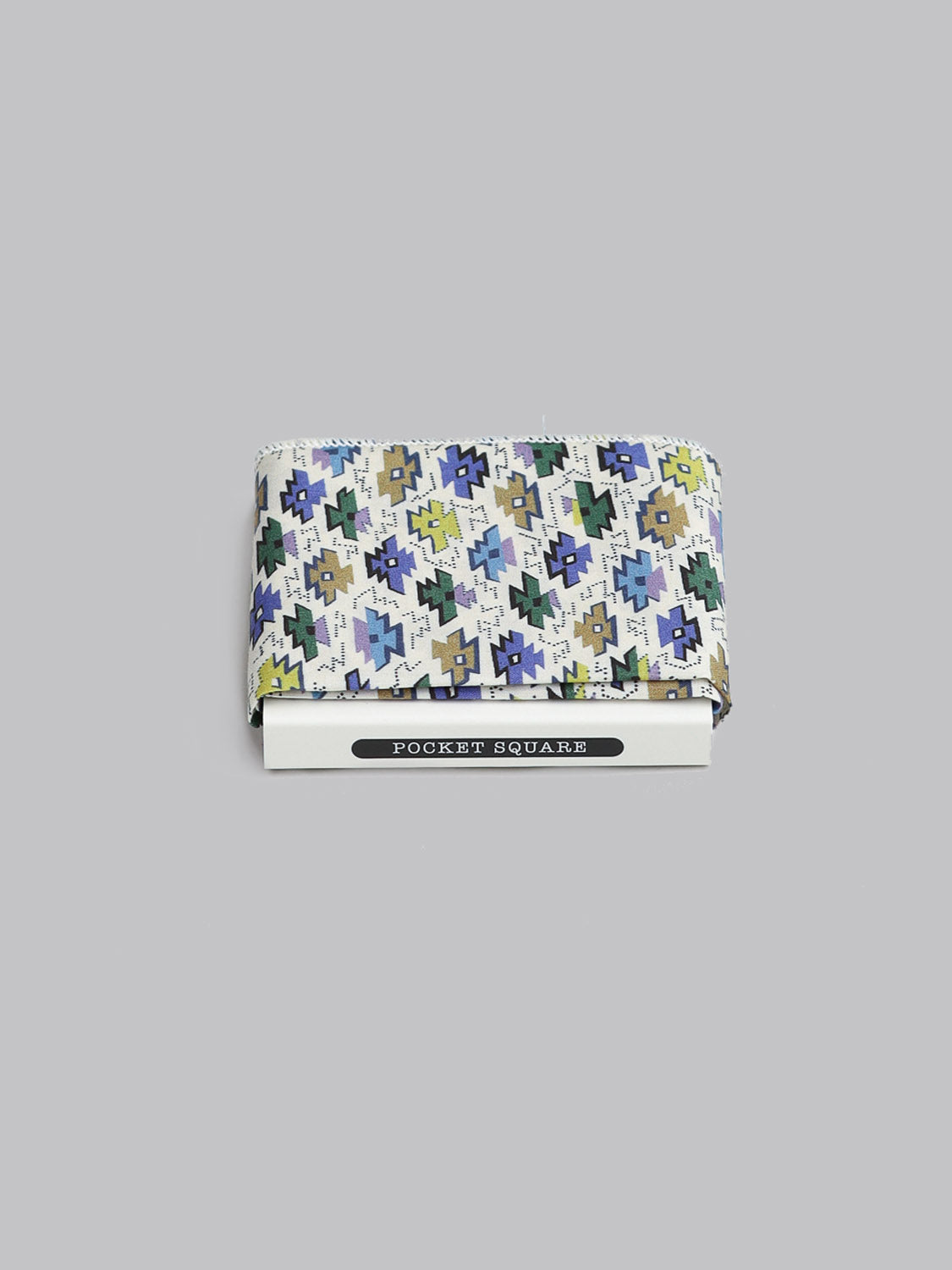 The Liberty™ Sunrise Pocket Square by ID Menswear, featuring a blue, green, beige, and white geometric pattern, is folded atop a white POCKET SQUARE box against a light gray background.