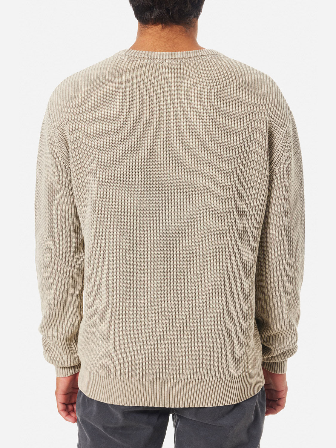 A person is seen from behind wearing the Katin Swell Sweater in beige, featuring long sleeves and ribbed details, paired with dark pants against a plain white background.