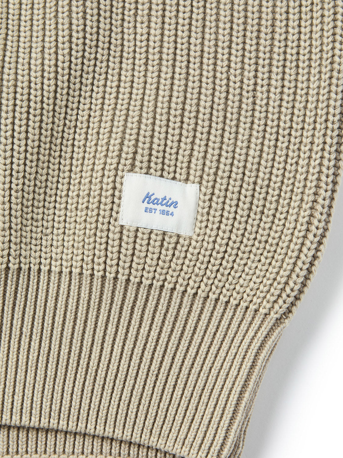 Close-up of the Katin Swell Sweater, a beige ribbed knit cotton piece featuring a small white rectangular label stitched on with blue "Katin EST 1954" text.