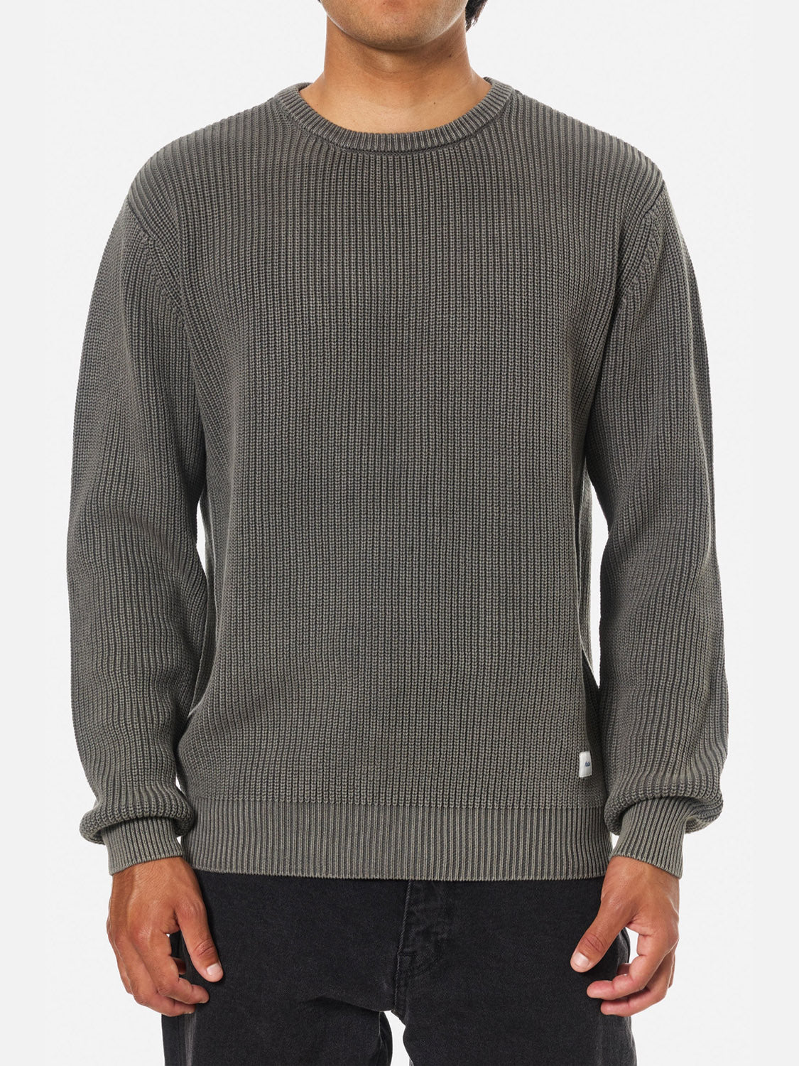 A person wears the Katin Swell Sweater, a ribbed long-sleeve crew neck in gray, with black pants, standing against a plain white background.