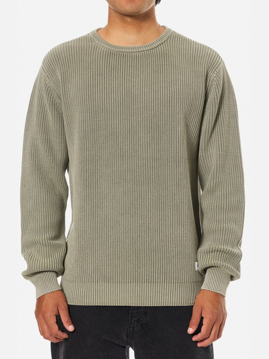A person wearing the Katin Swell Sweater—a light olive green, 100% cotton ribbed knit with long sleeves and a crew neckline—paired with black pants, stands against a plain white background.