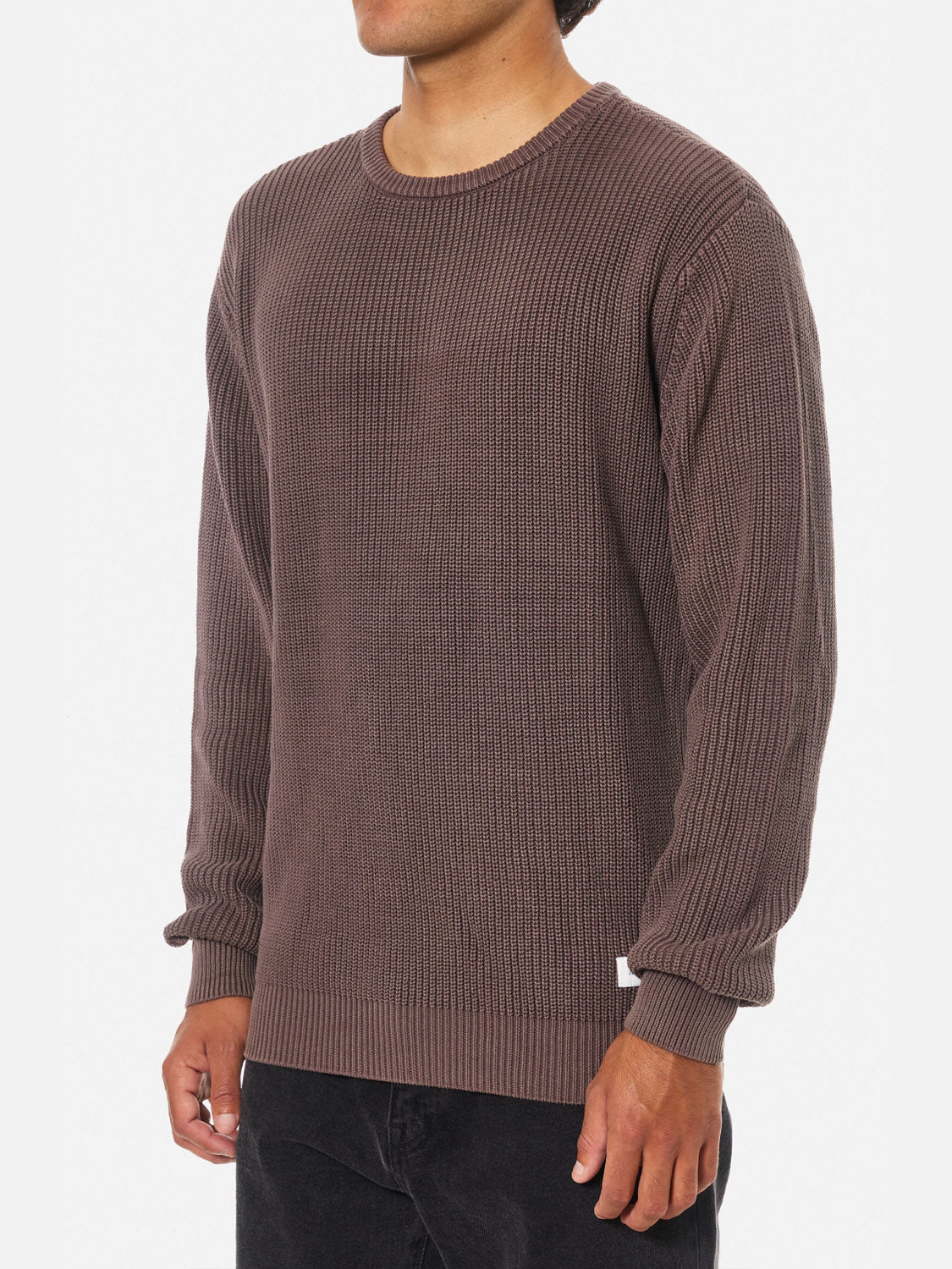 A person wearing the Katin Swell Sweater—a brown, long-sleeved, 100% cotton ribbed knit—paired with black pants stands against a plain white background, with their head out of frame.