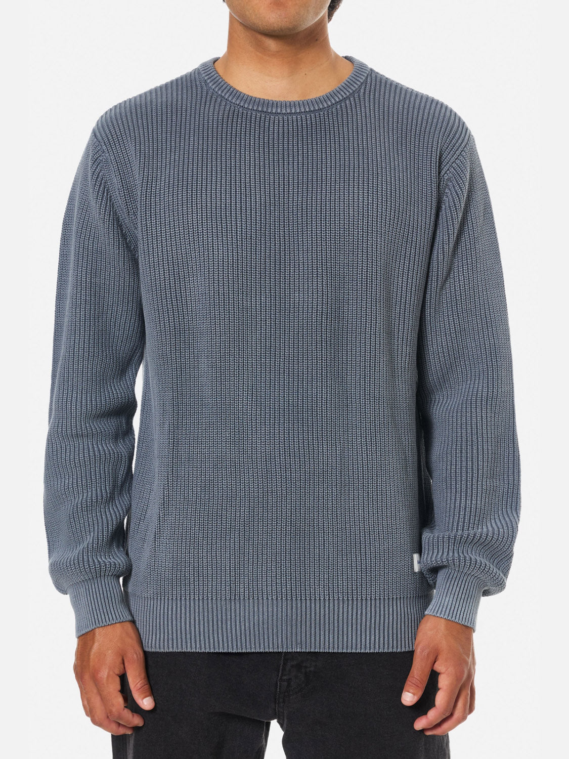 A person wears the Katin Swell Sweater, a textured cable knit in muted blue, with black pants, standing facing forward against a plain white background.
