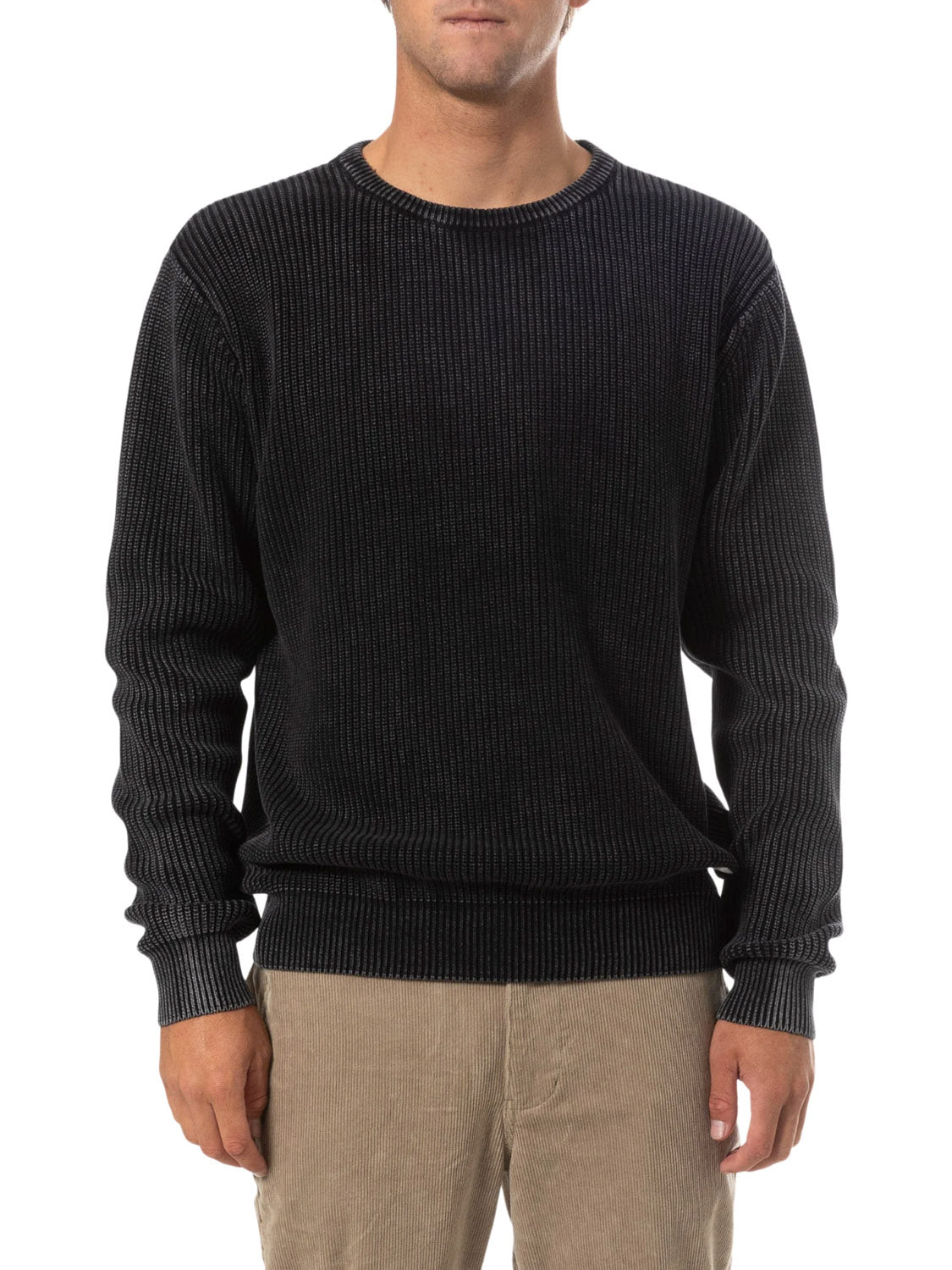 A person models the Katin Swell Sweater, a ribbed black cotton pullover, paired with beige corduroy pants against a plain white background. Their hands are relaxed at their sides and their face is partially out of frame.