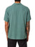 A person in a teal-green Katin Teller Shirt with a camp collar and black pants faces away. This Katin shirt, crafted from a comfy rayon-linen blend, offers a relaxed fit. They sport a tattoo on their left forearm stretching to the elbow.