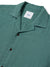 A close-up of the Katin Teller Shirt reveals a green hue with dark buttons and a neck label. Made from a rayon linen blend, it boasts a textured look and chic camp collar.