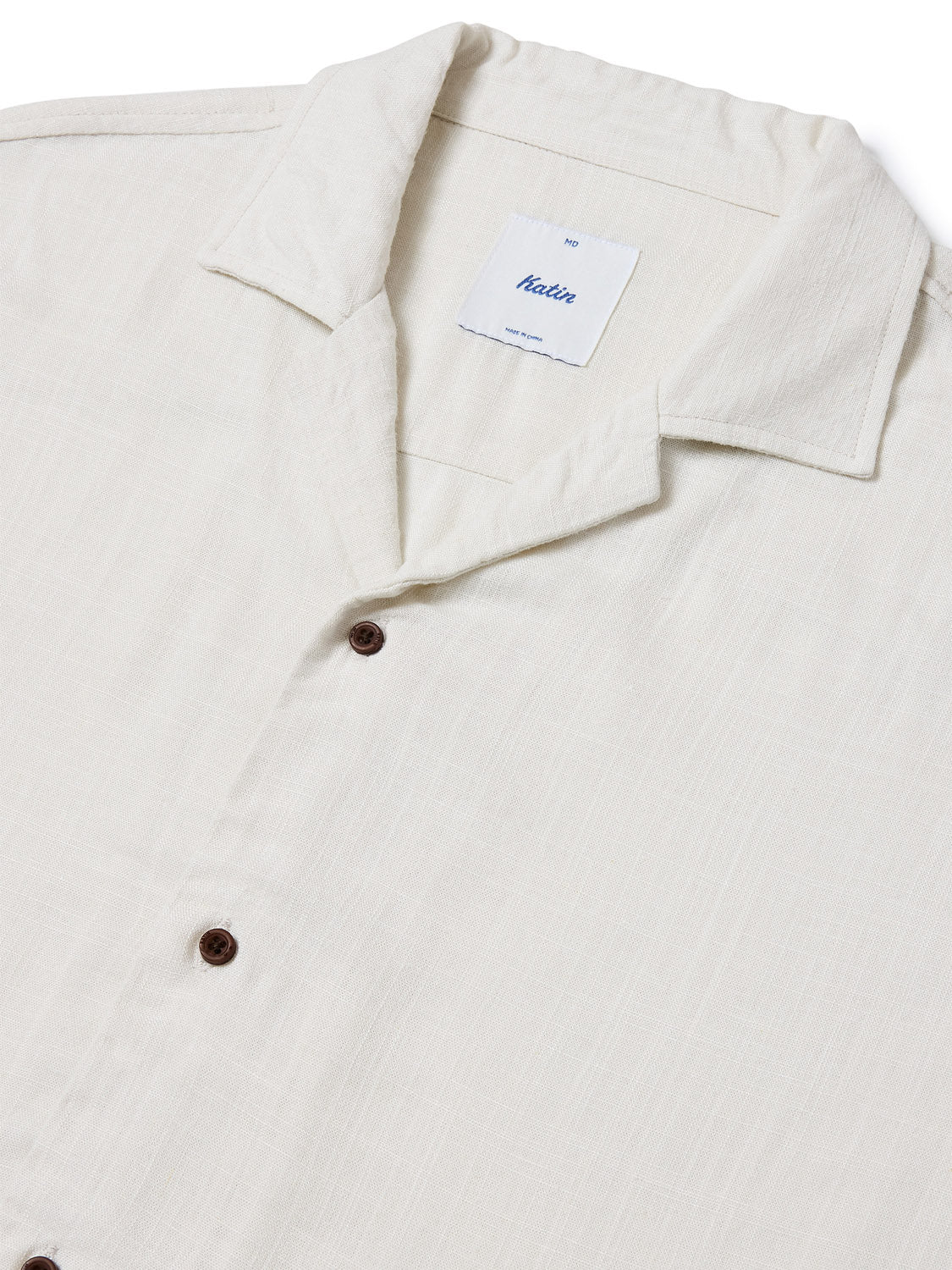 Close-up of a cream-colored Katin Teller Shirt featuring dark buttons, a camp collar, and a lightweight, subtly textured rayon linen blend. The white tag inside displays the Katin brand text.