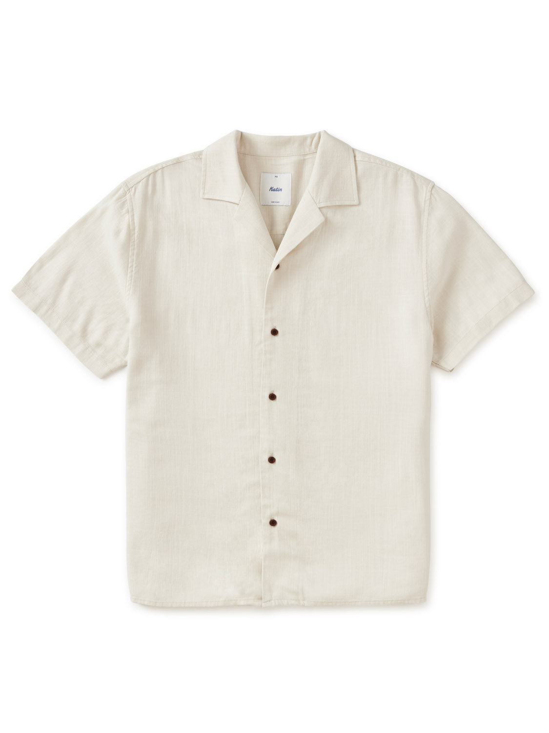 The Katin Teller Shirt, a luxurious rayon linen blend from Katin, offers a minimalist look with dark buttons, a relaxed camp collar, and beige short sleeves. Its effortless style is elegantly highlighted against a plain white background.