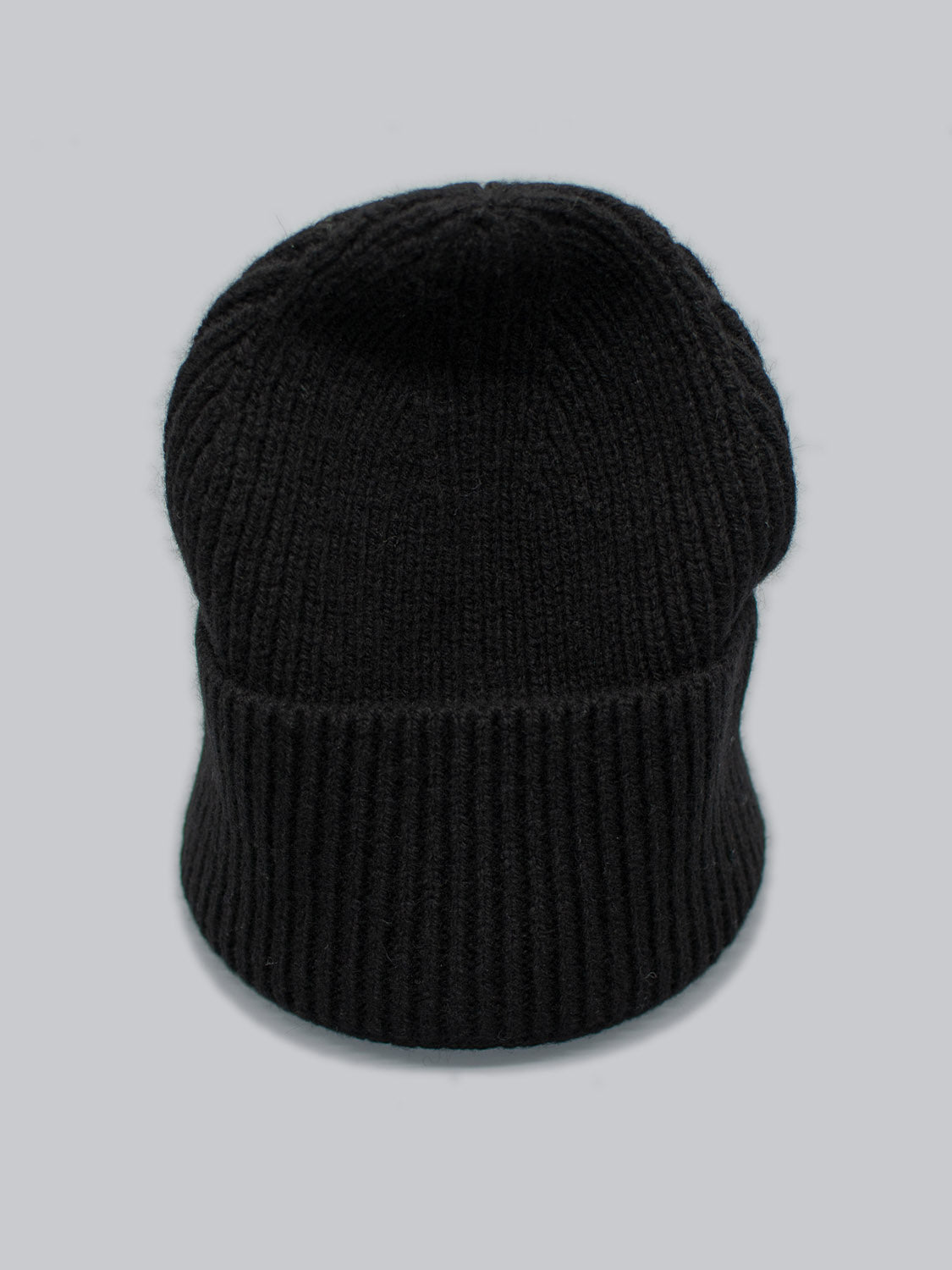 The Telluride Wool Beanie by ID Menswear, a black ribbed wool item, rests against a plain light gray background, highlighting its thick texture for cozy insulation and a comfortable fit.