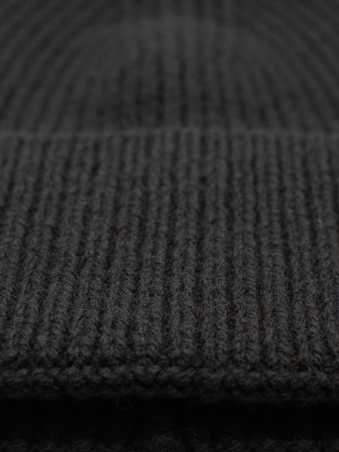 Close-up of the Telluride Wool Beanie by ID Menswear in dark gray, showing its ribbed texture. The soft, cozy fabric offers natural insulation with visible vertical stitching lines, highlighting the intricate knit pattern and comfortable fit.