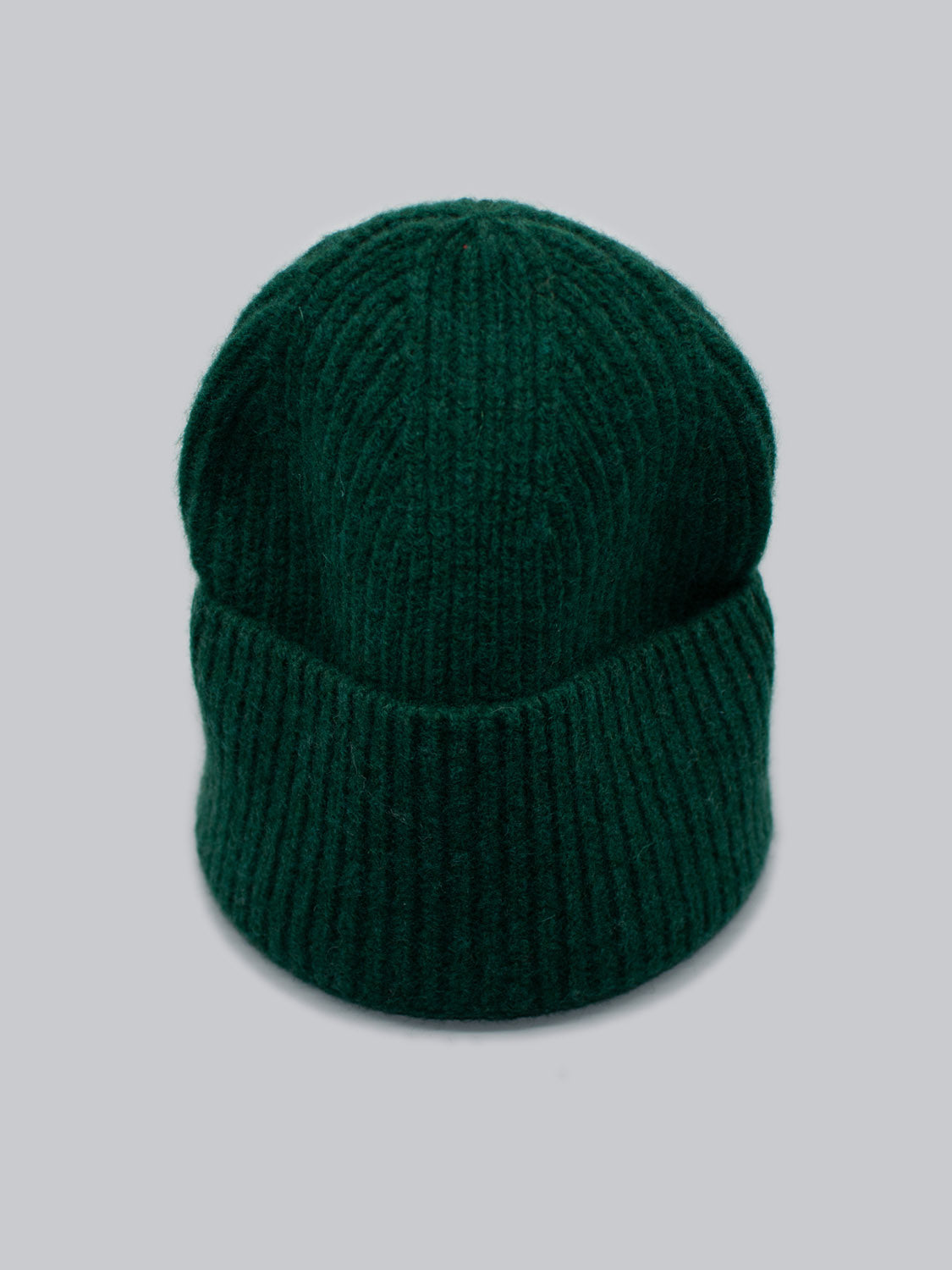 The Telluride Wool Beanie by ID Menswear is a dark green beanie with a folded brim, providing natural insulation and comfort, set against a plain gray background.