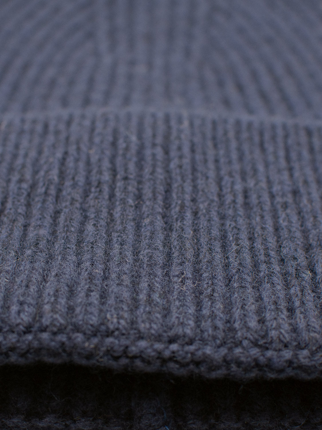 Close-up of the Telluride Wool Beanie by ID Menswear in dark gray. The ribbed knit fabric features fine vertical stitching for natural insulation, giving it a soft and warm texture.