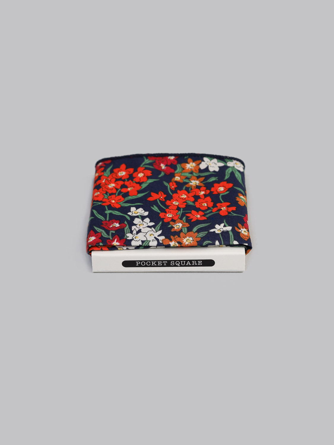 The Liberty™ Teresa Pocket Square by ID Menswear, made from Liberty of London Tana Lawn cotton, displays a vibrant red, white, and green floral pattern on dark fabric. It comes neatly boxed in white labeled POCKET SQUARE on a light gray background.
