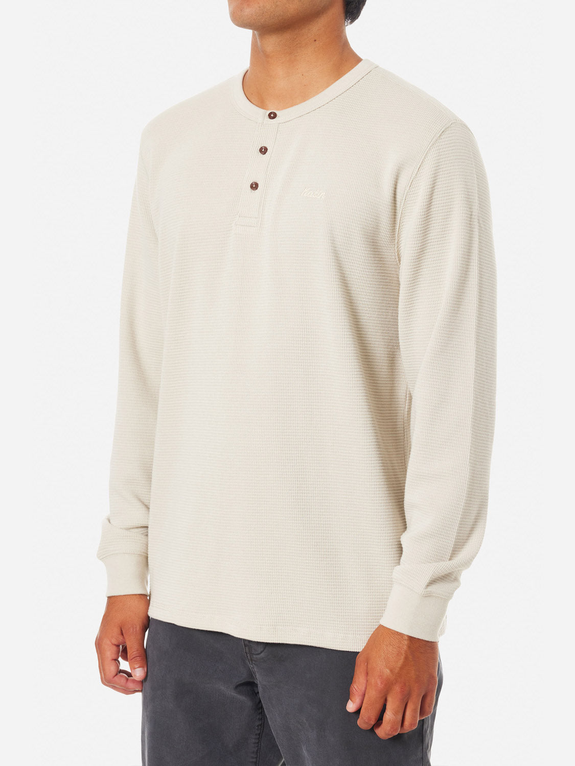 A person models a Katin Mesa Thermal in cream, a 3-button Henley made from a cotton-polyester blend featuring subtle textures, set against a white background. Dark pants complete the look, but their face is not visible.
