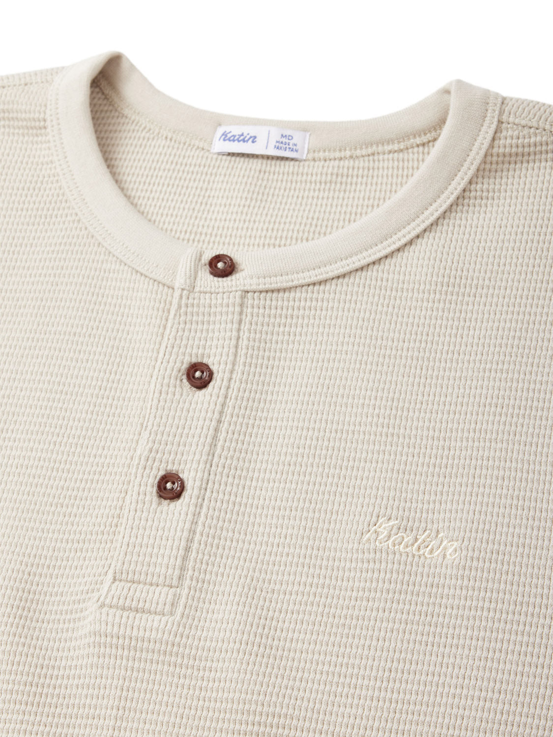 Close-up of the Katin Mesa Thermal in beige, showcasing a waffle-knit texture with three brown buttons and a small embroidered logo on the left chest. Made from a cotton-polyester blend, it combines style and comfort for everyday wear.