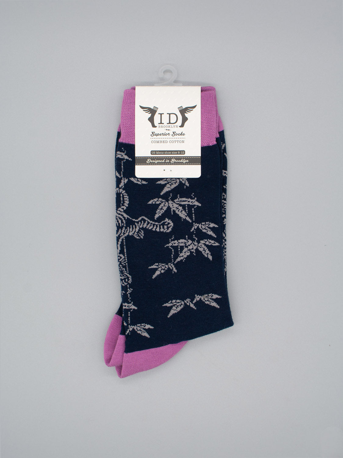 A pair of limited edition Tiger Graphic Socks by ID Menswear, featuring dark blue with white leaf patterns and pink accents at the toes and heels, crafted from soft combed cotton and displayed with a label against a gray background.