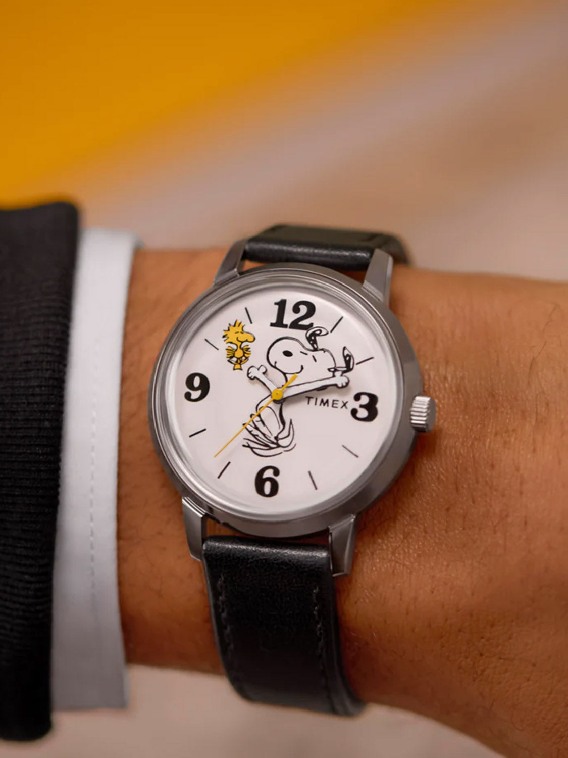 A person wears the Timex x Peanuts® Marlin® 75th Anniversary Edition 38mm Leather Strap Watch, featuring Snoopy and Woodstock on the white dial with Snoopys arms as watch hands—a charming tribute from Timex.