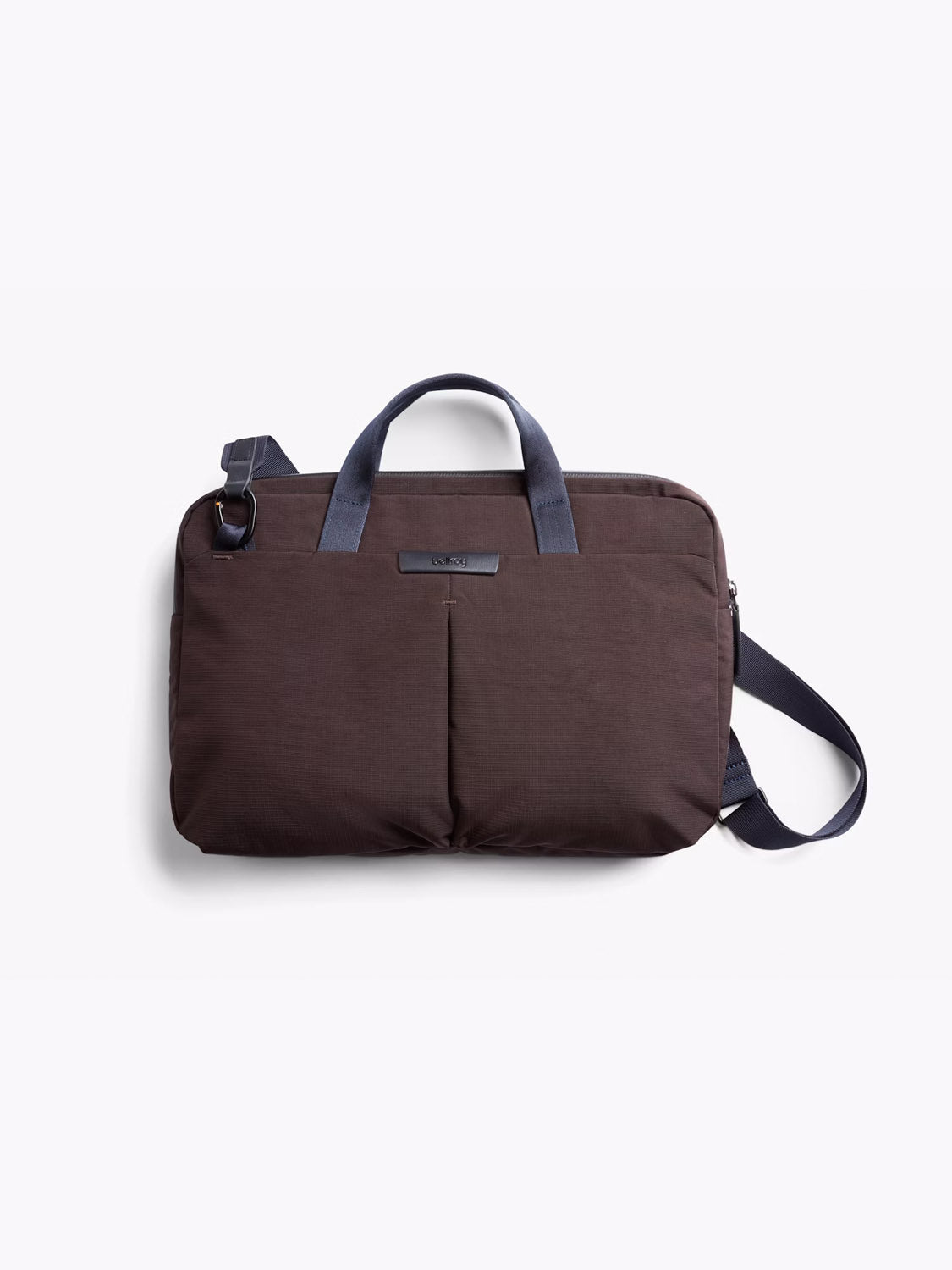 The Bellroy Tokyo Work Bag - 20L is a brown commuter bag with two front pockets, navy handles, a detachable navy shoulder strap, and a 16" laptop sleeve, shown against a plain white background.