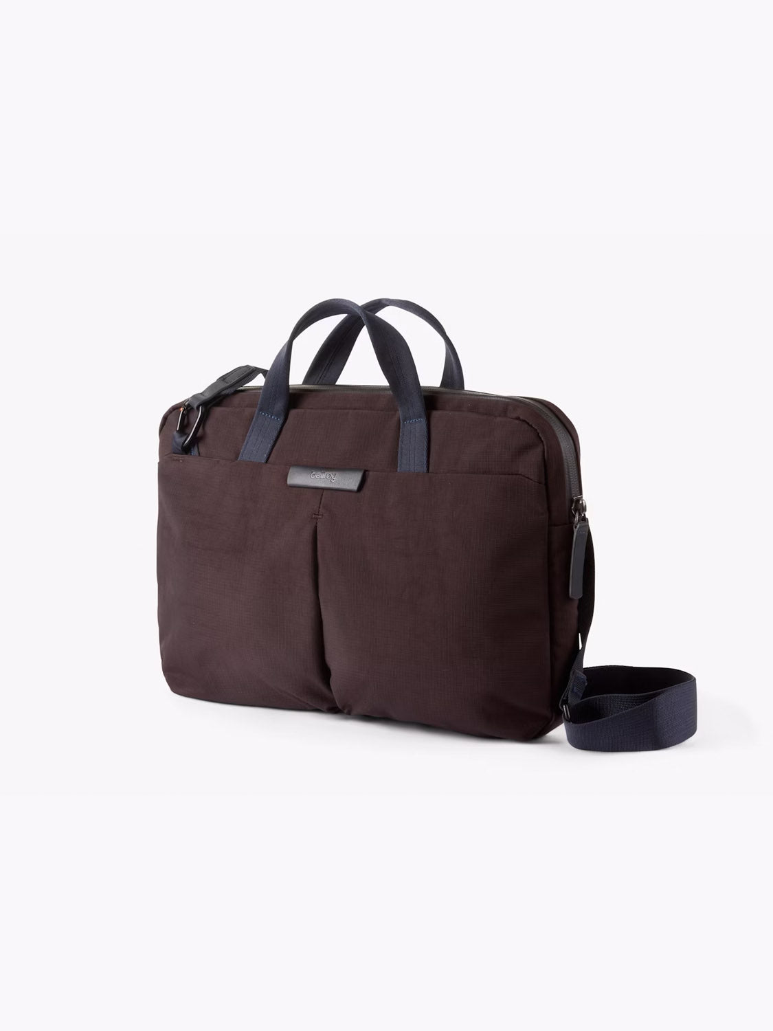 The Bellroy Tokyo Work Bag - 20L is a dark brown commuter bag with navy handles, two front pockets, a detachable shoulder strap, and a 16" laptop sleeve, shown against a plain light background.