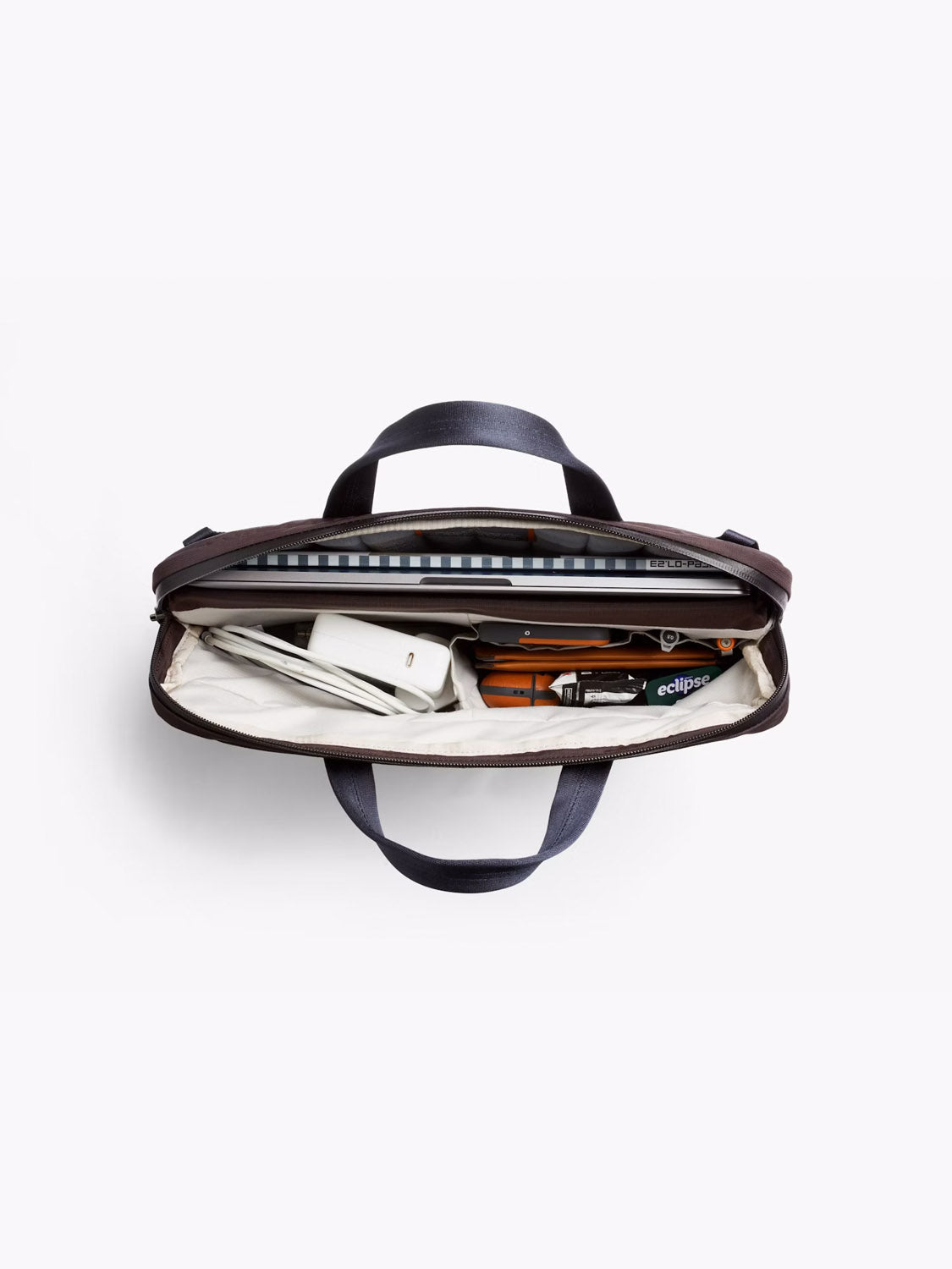 Top view of the Bellroy Tokyo Work Bag - 20L, open to show organized contents like a 16” laptop sleeve, notebook, phone, pens, and office items. Features striped lining and two dark handles.