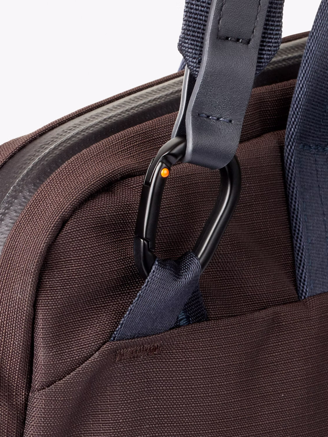 Close-up of the Bellroy Tokyo Work Bag - 20L in brown recycled fabric, featuring a navy strap, black carabiner, visible seam and zipper. Designed for professional commuters and fits a 16” laptop sleeve.