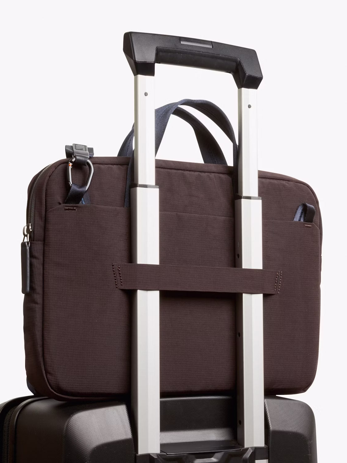 A close-up shows the Bellroy Tokyo Work Bag - 20L, securely strapped over a black suitcase with an extended telescopic handle using its back sleeve.