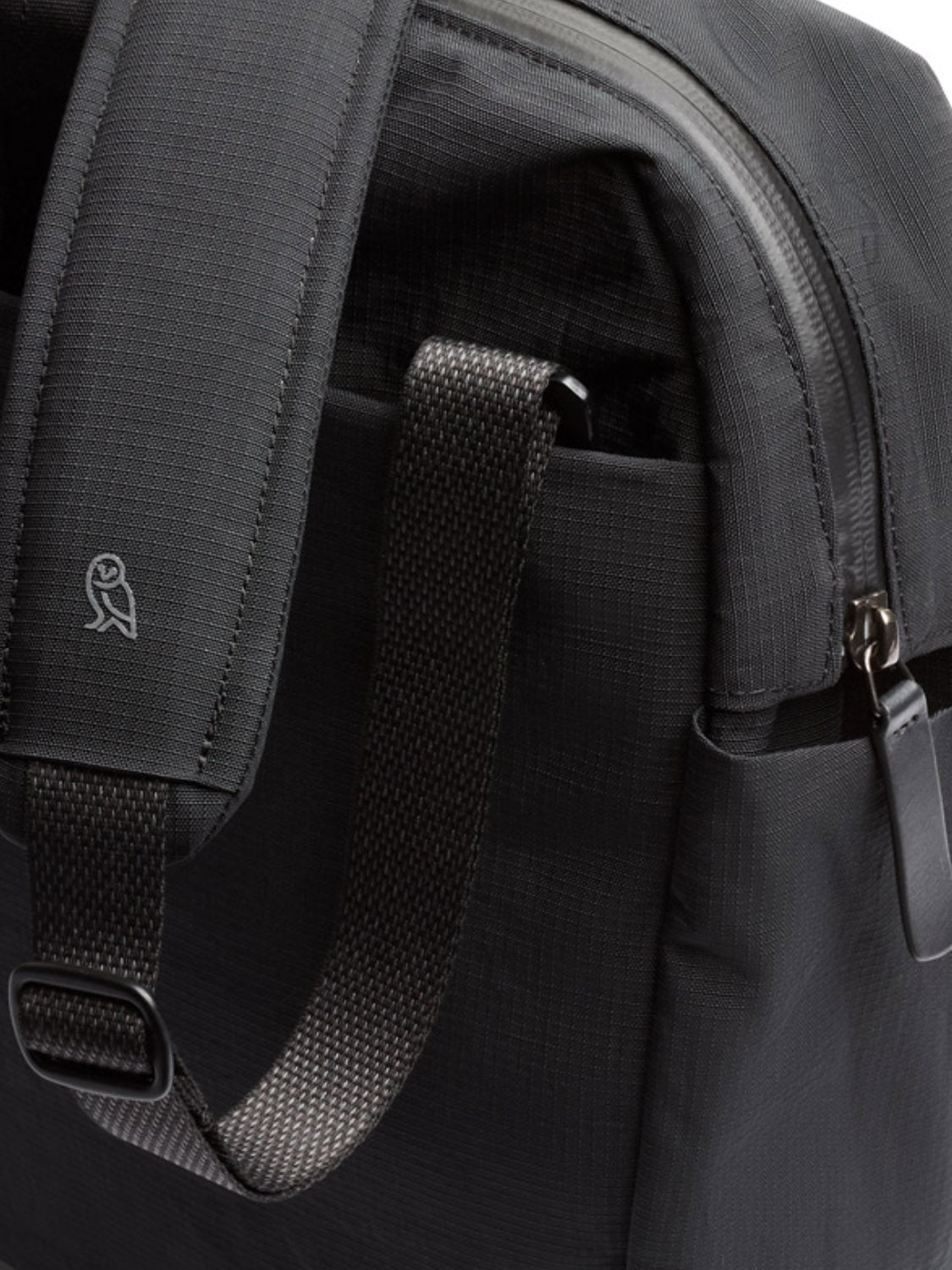 Close-up of the Bellroy Tokyo Work Bag - 20L in dark grey recycled fabric, showing its textured shoulder strap with stitched owl logo, webbing handle, metal zipper, and a 16” laptop sleeve—ideal for professionals.