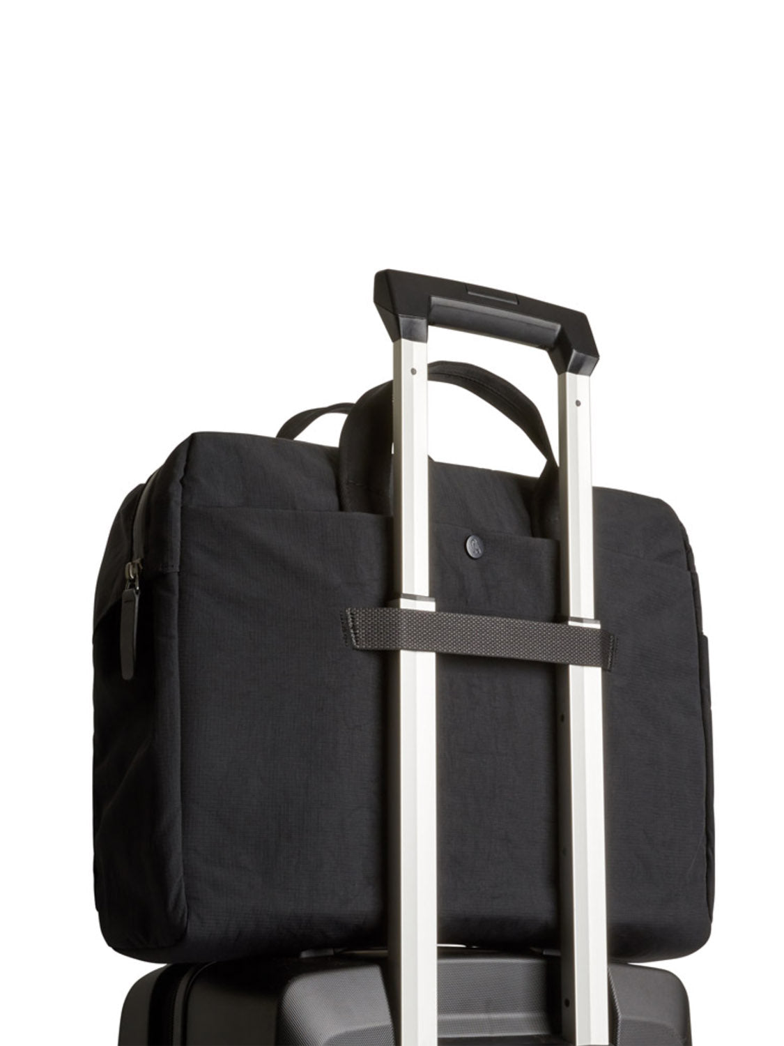 The Bellroy Tokyo Work Bag - 20L, designed to fit a 16” laptop sleeve and featuring short handles, is securely attached to the extended handle of a rolling suitcase against a plain white background.