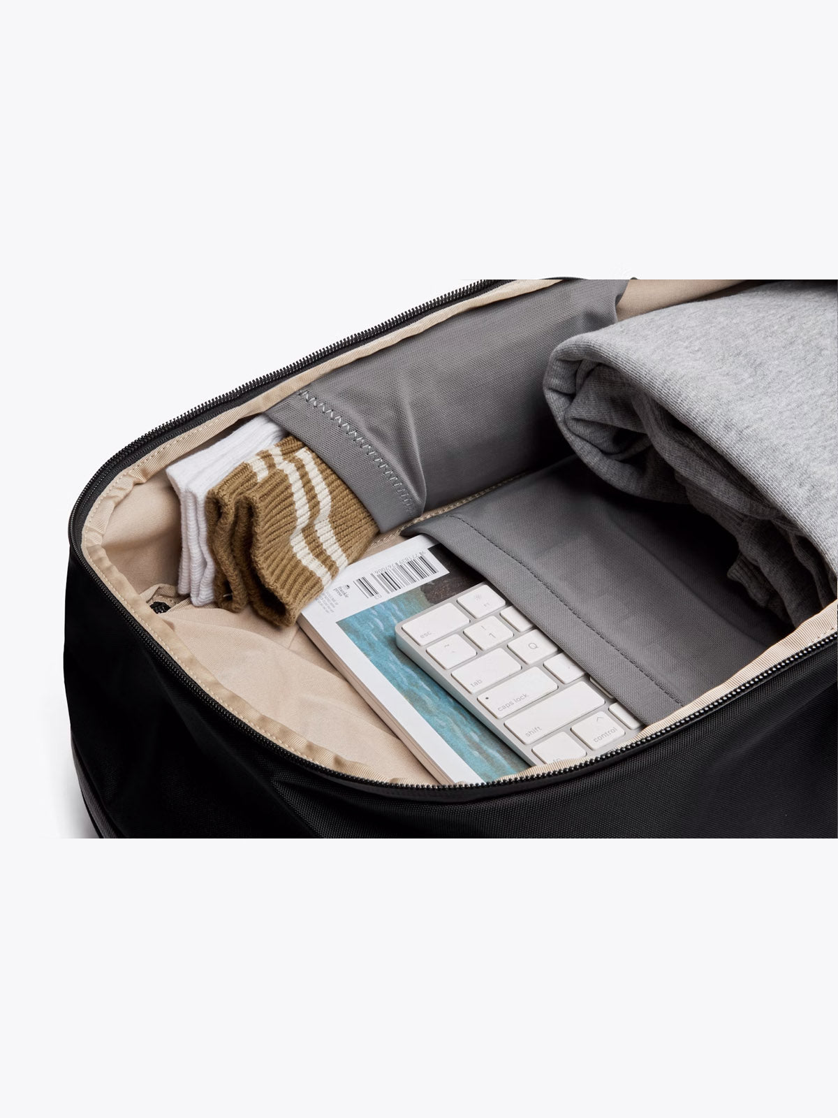 The Bellroy Transit Workpack - 20L showcases a minimalist, organized interior with separate compartments for folded clothes, striped socks, a white keyboard, book, and boarding pass. A laptop sleeve enhances its functionality as the ideal work bag.