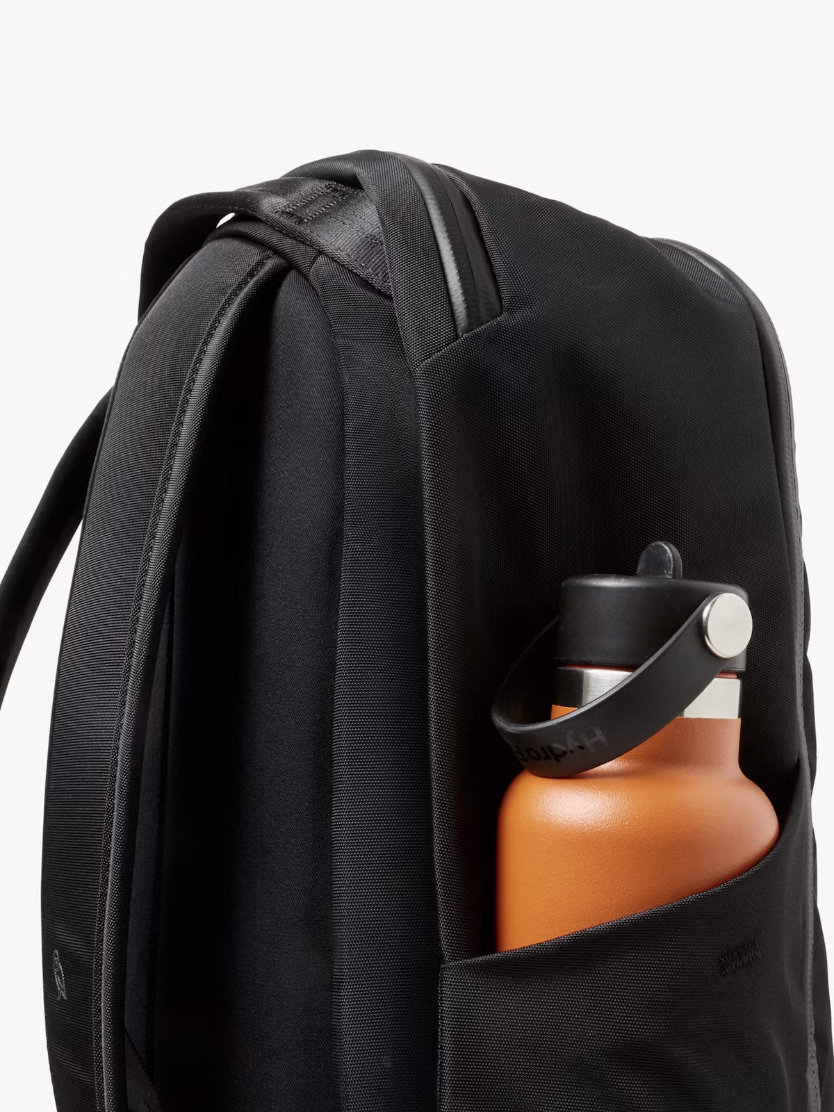 The Bellroy Transit Workpack - 20L is a minimalist black bag with padded shoulder straps, a laptop sleeve, and a side pocket for carrying an orange water bottle with a black lid.